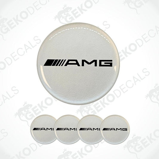 A set of four white vinyl stickers with the AMG (Alternate Mercedes-Benz) logo on them. The stickers are designed to be used on car wheel caps.