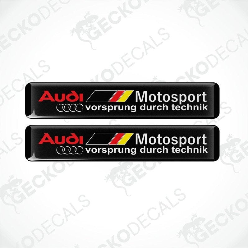 Two black vinyl stickers with red, white, and yellow Audi Motosport branding, placed on a white background.