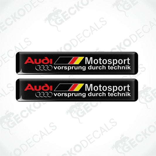 Two black vinyl stickers with red, white, and yellow Audi Motosport branding, placed on a white background.