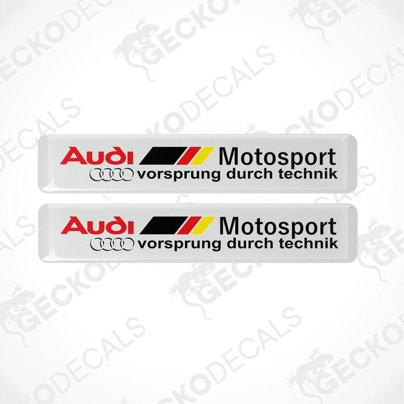 Two white vinyl stickers with red, black, and yellow Audi Motosport branding, placed on a white background.