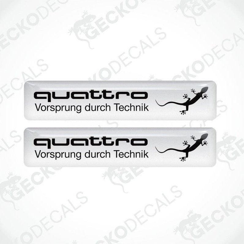 Two white vinyl decals with 'quattro Vorsprung durch Technik' and a black Audi logo on a white background.