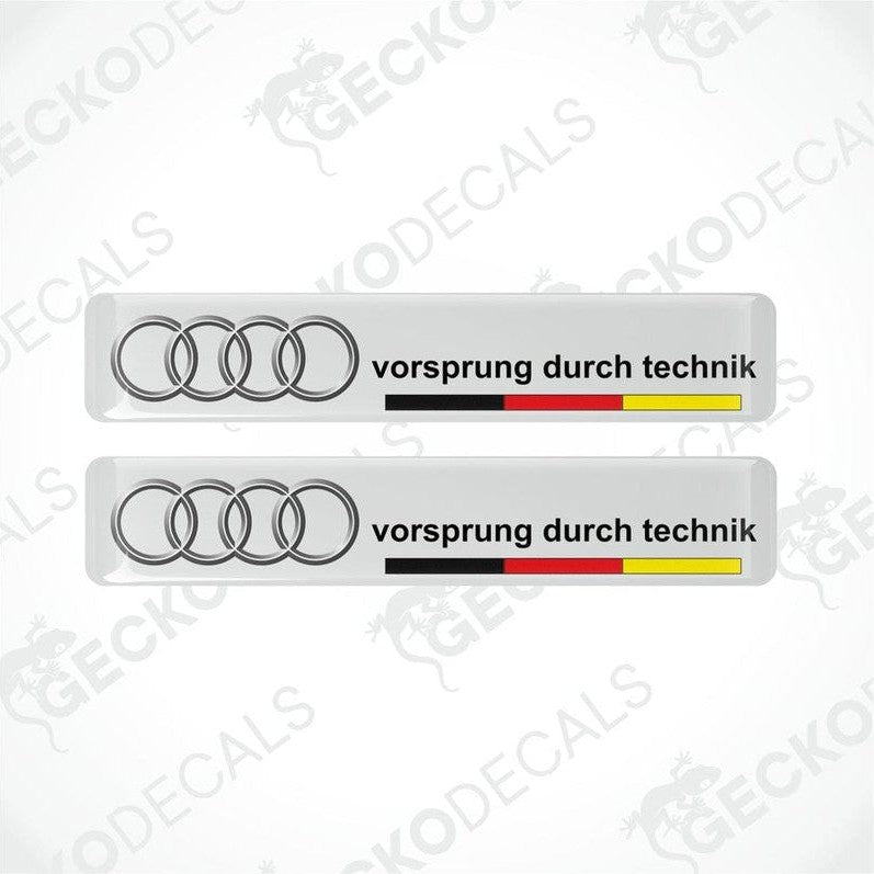 Two white vinyl decals with the text 'vorsprung durch technik' and the Audi logo in silver, arranged horizontally.