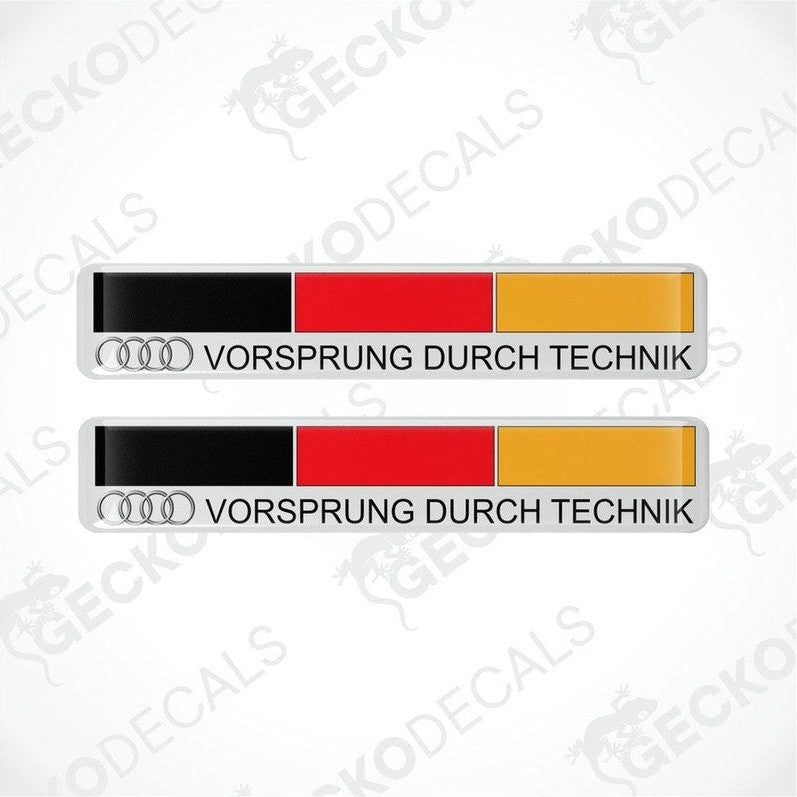 Two rectangular car decals with 'VORSprung DURCH TECHnik' text and the Audi logo, predominantly white with red and yellow stripes.
