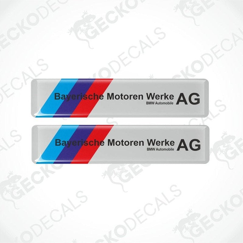 Two rectangular car decals with a striped pattern in blue and red on a white background, and black text saying 'Bayerische Motoren Werke AG BMW Automobile AG'.