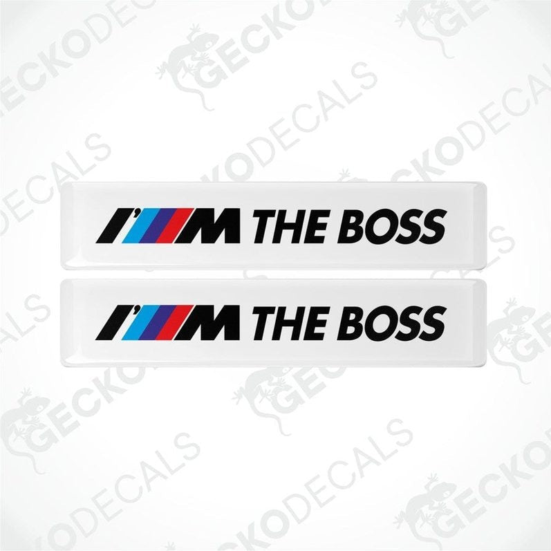 Two withe rectangular car decals with the text 'THE BOSS' and the BMW logo in black, red, and blue.