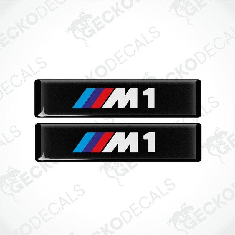 Two stickers with BMW M1 logos in light blue, blue and red on a black background