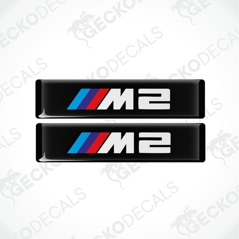 Two stickers with BMW M2 logos in light blue, blue and red on a black background