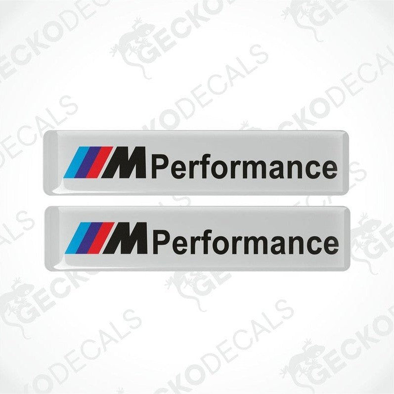 Two rectangular white vinyl decals with 'M Performance' text and the BMW logo in red, blue, and black.