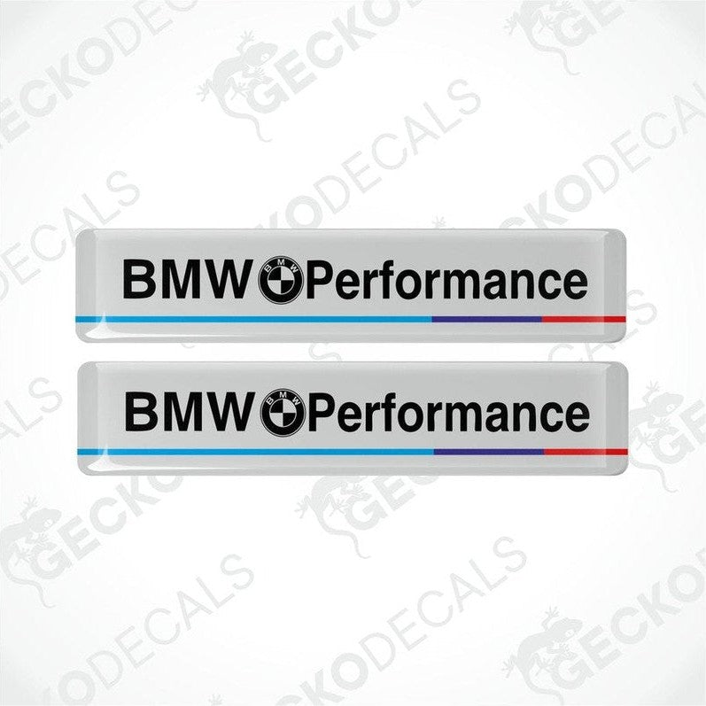 Two rectangular white vinyl decals with 'BMW Performance' text, one with a red stripe and one with a blue stripe.