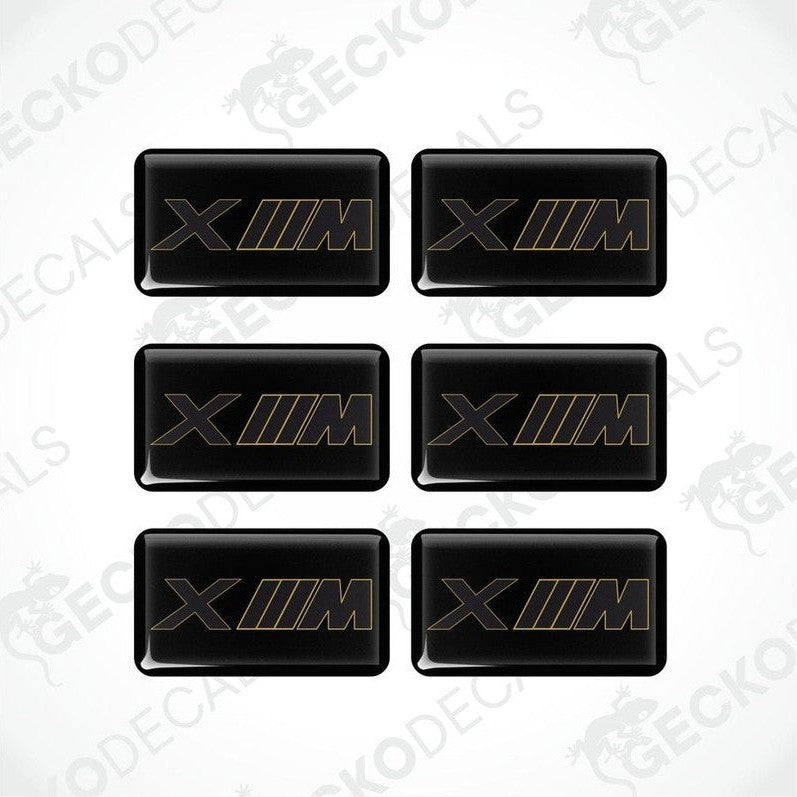 A set of six black vinyl stickers with the BMW XM logo in gold.