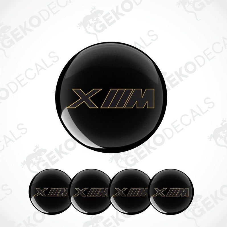 Set of four black vinyl decals with 'XM' logo in gold, intended for use on vehicle wheels.