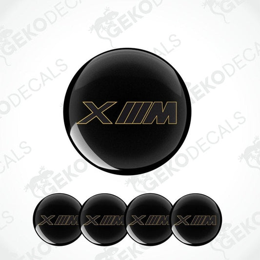 Set of four black vinyl decals with 'XM' logo in gold, intended for use on vehicle wheels.