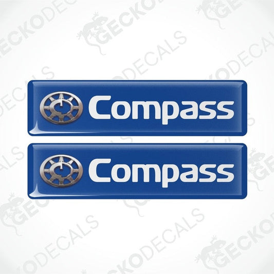 Two blue vinyl stickers with a compass logo, designed for use on vehicle windows.
