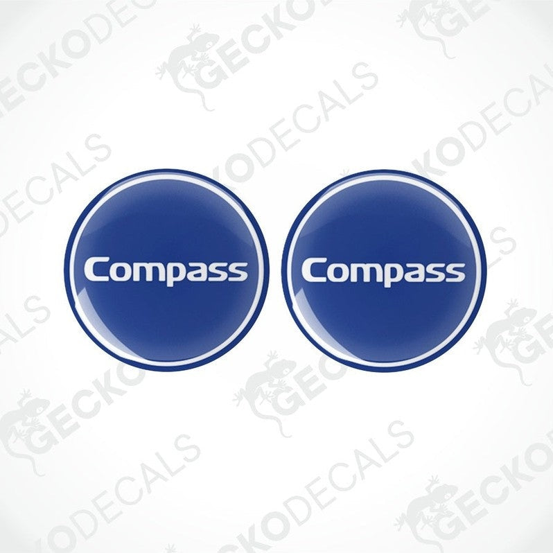 Two blue vinyl decals with the word 'Compass' printed on them, placed against a white background.