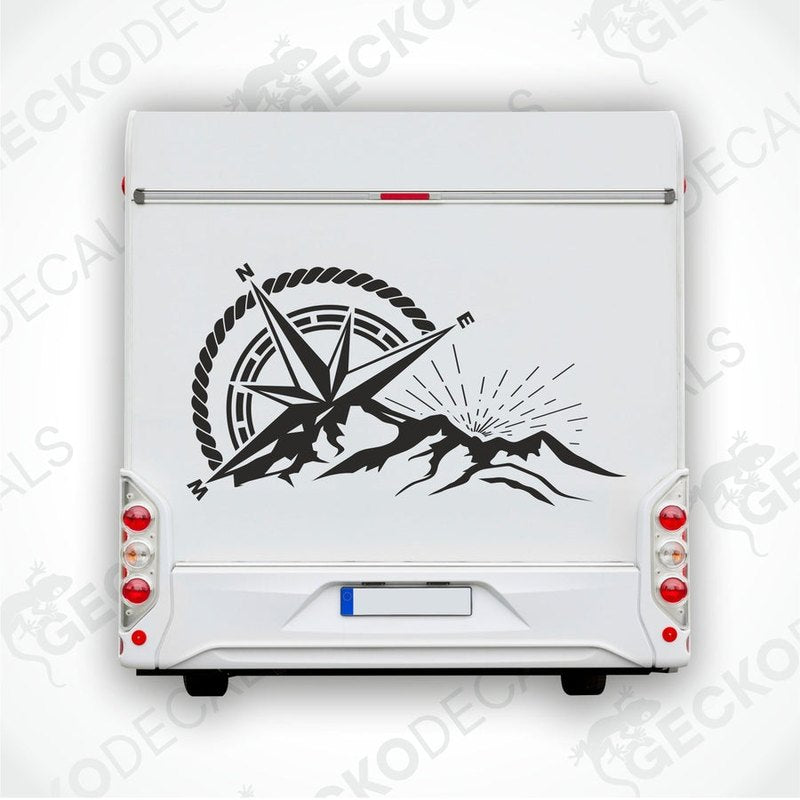 A black and white die cut decal of a compass with mountains and a sun in the center, displayed on a white vehicle.