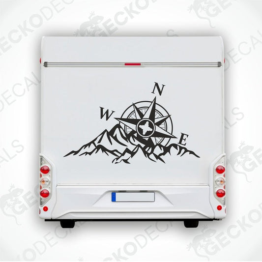 A white caravan with a black decal featuring a compass and mountains. The decal is positioned on the rear side of the caravan, near the window.