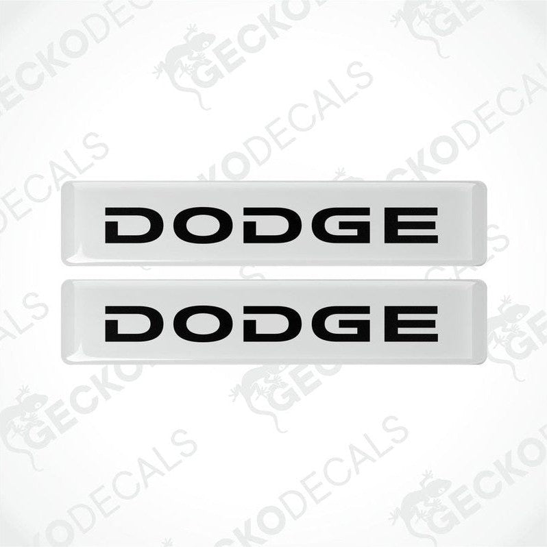 Two white and white vinyl stickers with the word "DODGE" printed in black.
