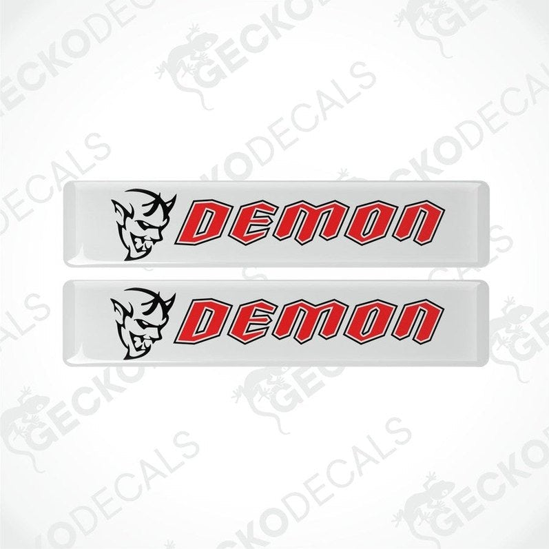 Two white vinyl stickers with the word 'DEMON' written in red. One sticker has a graphic of a demon above the text, and both are branded with 'GECKODECALS'.