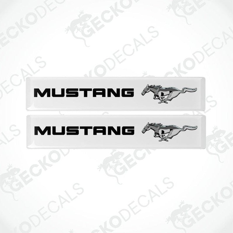 Two white vinyl stickers with the word 'MUSTANG' and an image of a horse and rider on them, placed against a white background.