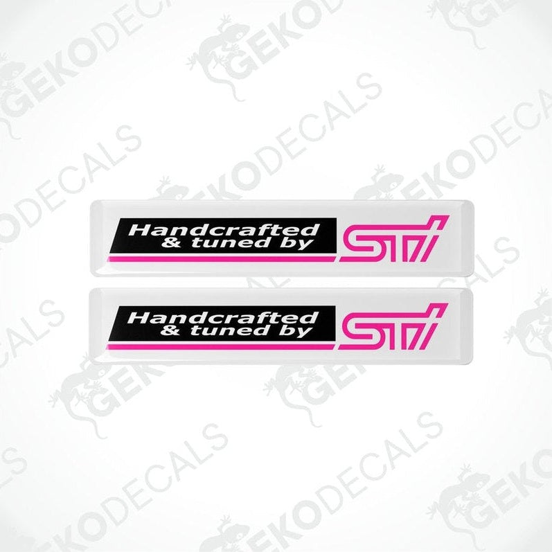 Two white vinyl stickers with 'HANDCRAFTED & TUNED BY STI' text, featuring a pink and black color scheme.
