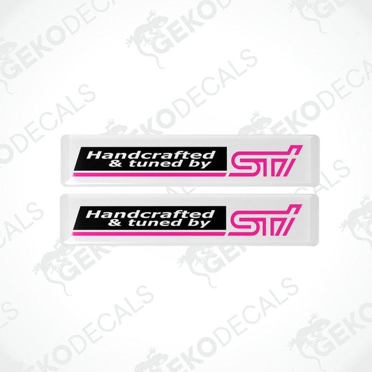 Two white vinyl stickers with 'HANDCRAFTED & TUNED BY STI' text, featuring a pink and black color scheme.