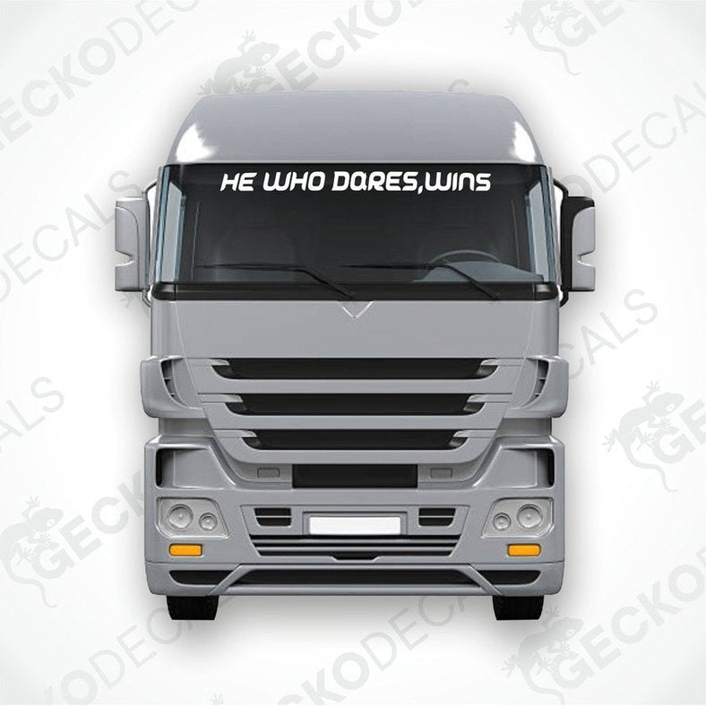 A die cut decal with the phrase 'HE WHO DARES, WINS' positioned on the front window of a gray truck.