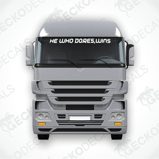A die cut decal with the phrase 'HE WHO DARES, WINS' positioned on the front window of a gray truck.