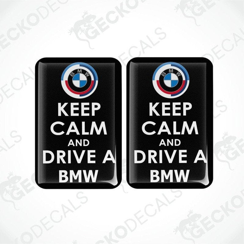 Two rectangular black vinyl decals with the text 'KEEP CALM AND DRIVE A BMW' and the BMW logo in white and red.