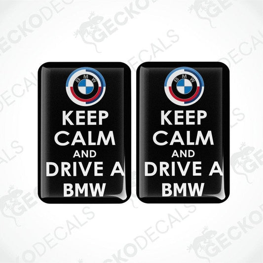 Two rectangular black vinyl decals with the text 'KEEP CALM AND DRIVE A BMW' and the BMW logo in white and red.