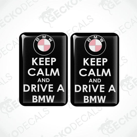 Two rectangular black vinyl decals with the text 'KEEP CALM AND DRIVE A BMW' and the BMW logo in pink.