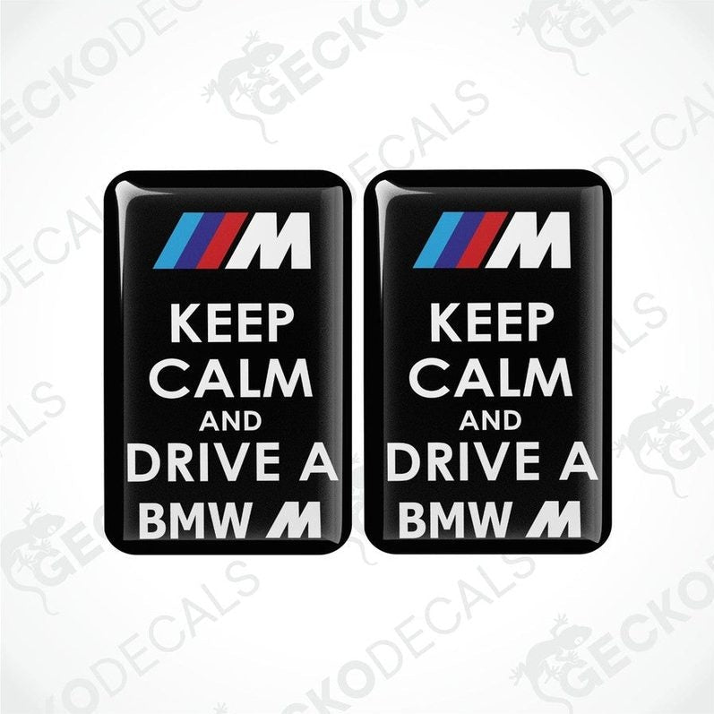 Two rectangular black vinyl decals with the text 'KEEP CALM AND DRIVE A BMW M' in white and red letters, featuring the BMW M logo.