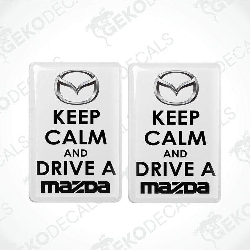 Two white vinyl stickers with the text 'KEEP CALM AND DRIVE A MAZDA' and the Mazda logo.