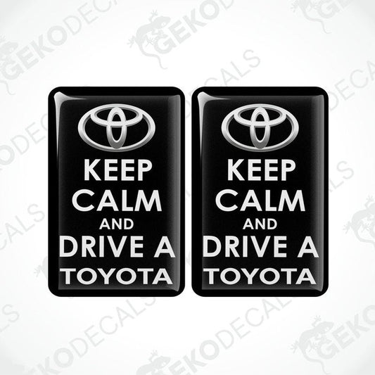 Two rectangular black vehicle decals with white text that read 'KEEP CALM AND DRIVE A TOYOTA', including the Toyota logo.