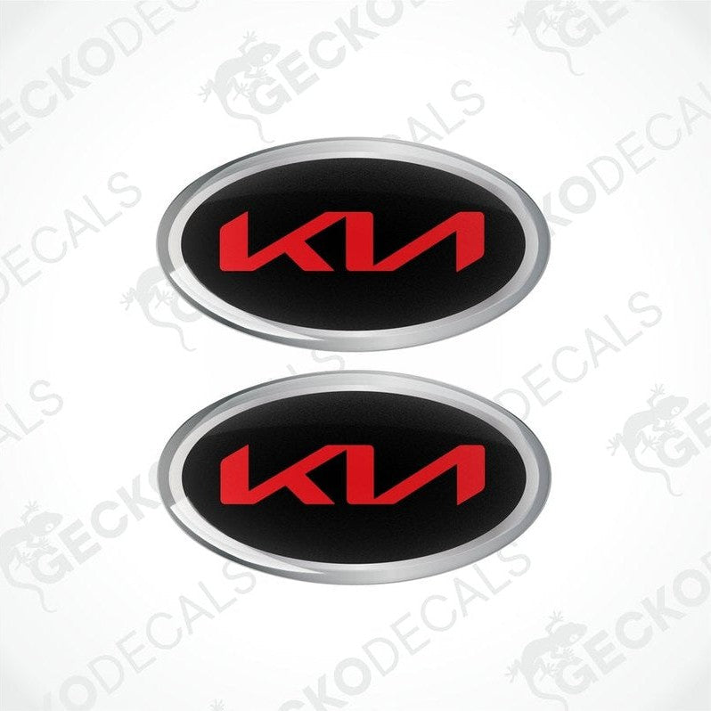 Two oval-shaped vinyl decals with 'KIA' written in bold letters, predominantly red with black and silver accents.