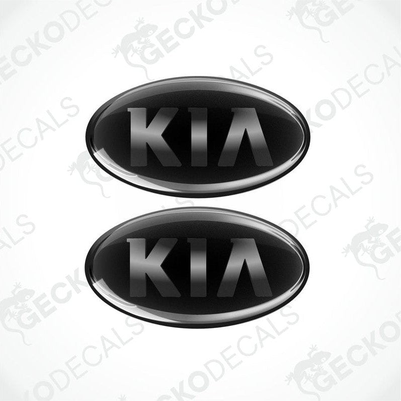 Two black oval-shaped vinyl decals with the KIA brand logo in white text.