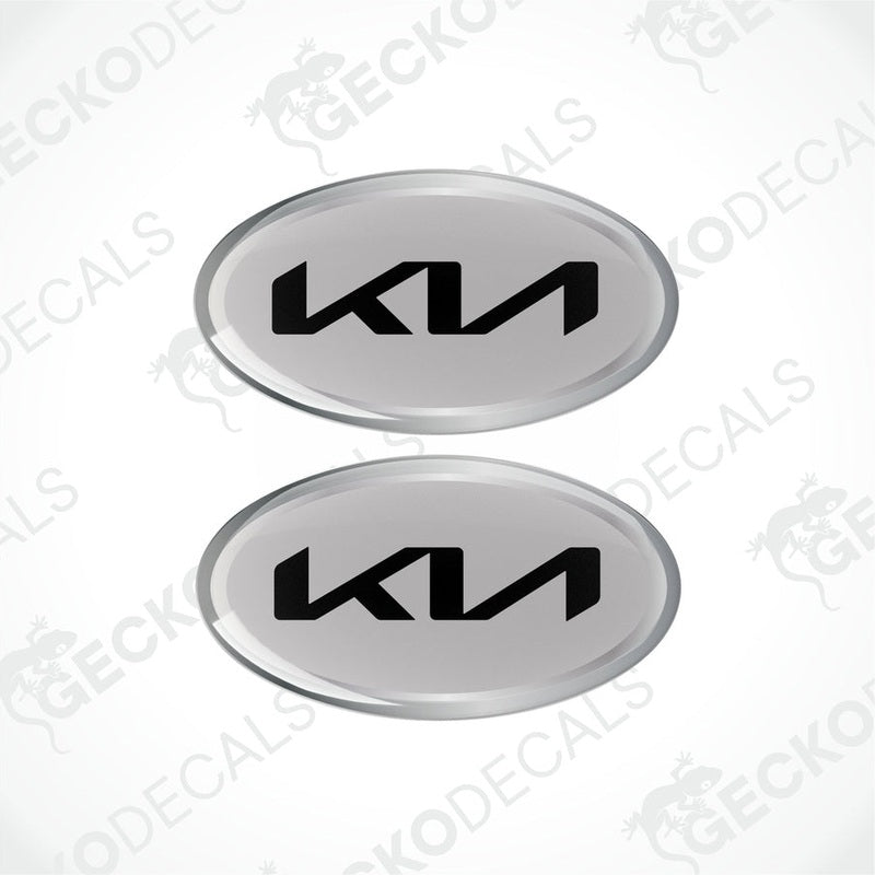 Two oval-shaped vinyl decals with 'KIA' written in bold letters, predominantly grey with black and silver accents.