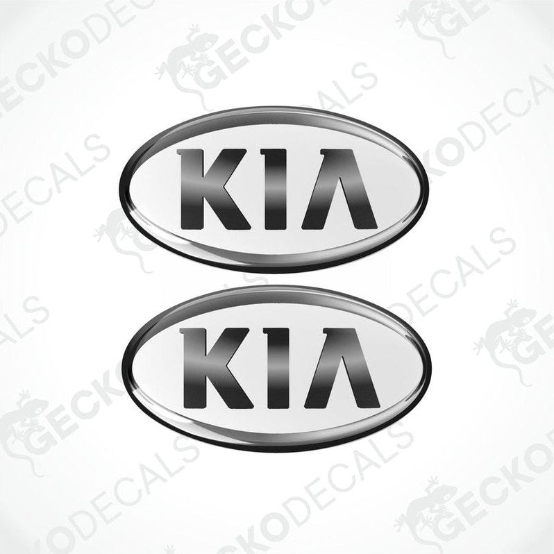 Two white oval-shaped vinyl decals with the KIA brand logo in dark grey text.