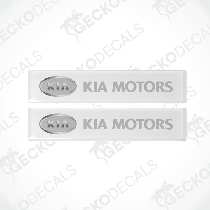 Two white rectangular car decals with 'KIA MOTORS' written in grey text.