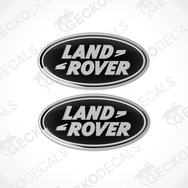 Two oval-shaped black and silver car decals with the text 'LAND ROVER' on them.