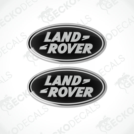 Two oval-shaped black and silver car decals with the text 'LAND ROVER' on them.