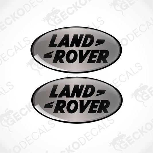 Two oval-shaped black and silver vinyl decals with the text 'LAND ROVER' on them.
