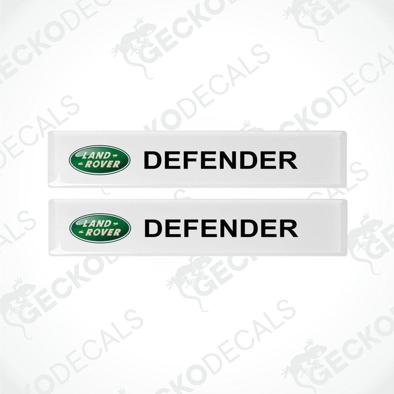 Two white vinyl decals with the text 'DEFENDER' and the Land Rover logo in green.