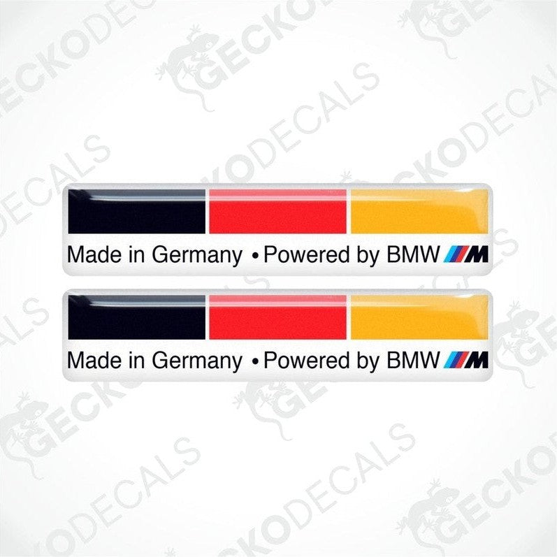 Two vinyl stickers with the words "MADE IN GERMANY POWERED BY BMW", on a white background and in the colors of the German flag.