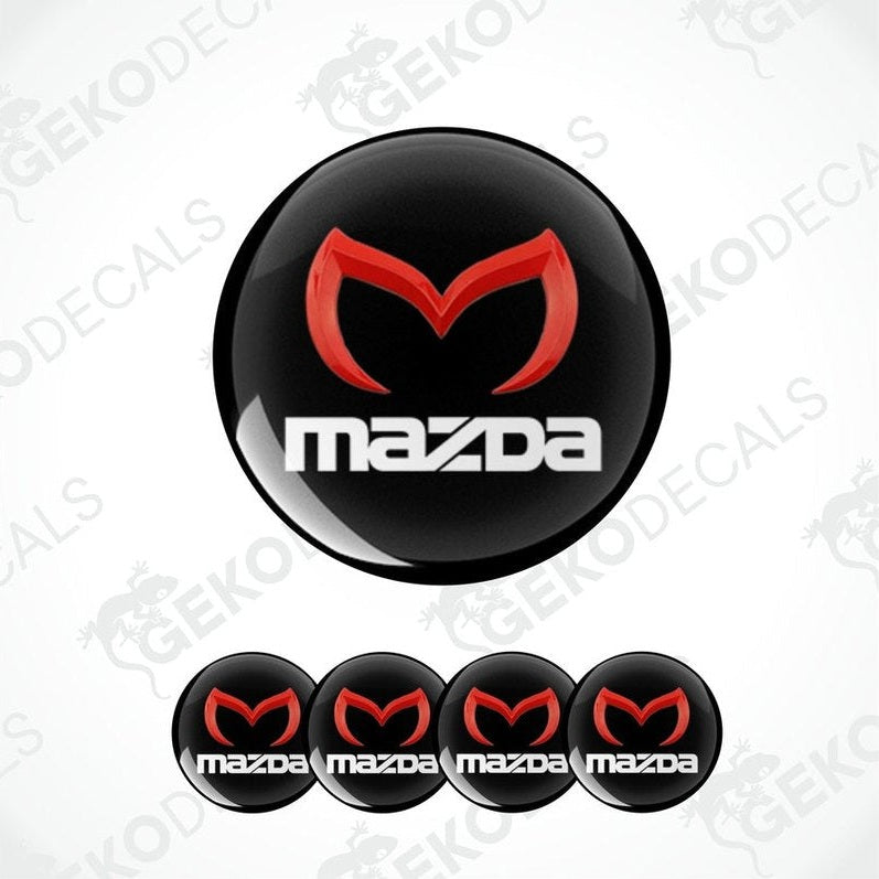 A set of four black vinyl stickers with a red and white MAZDA logo, designed for use on car wheels.