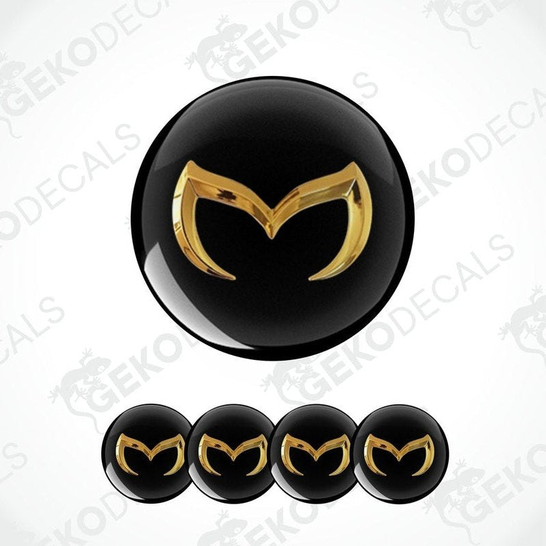 Set of four black and gold Mazda car wheel decals and one emblem decal.