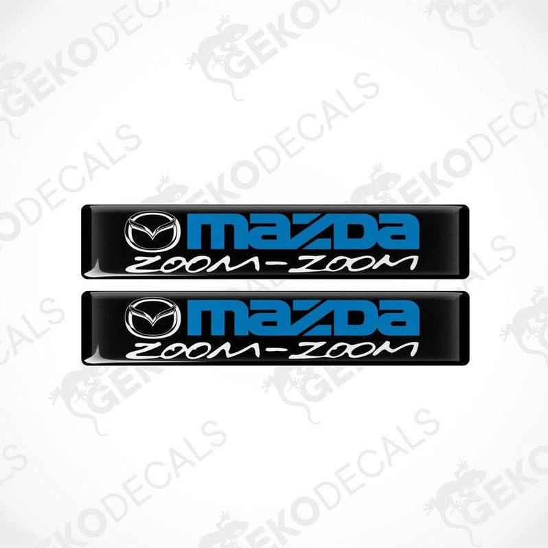 Two black vinyl stickers with the text 'MAZDA ZOOM-ZOOM' in blue.