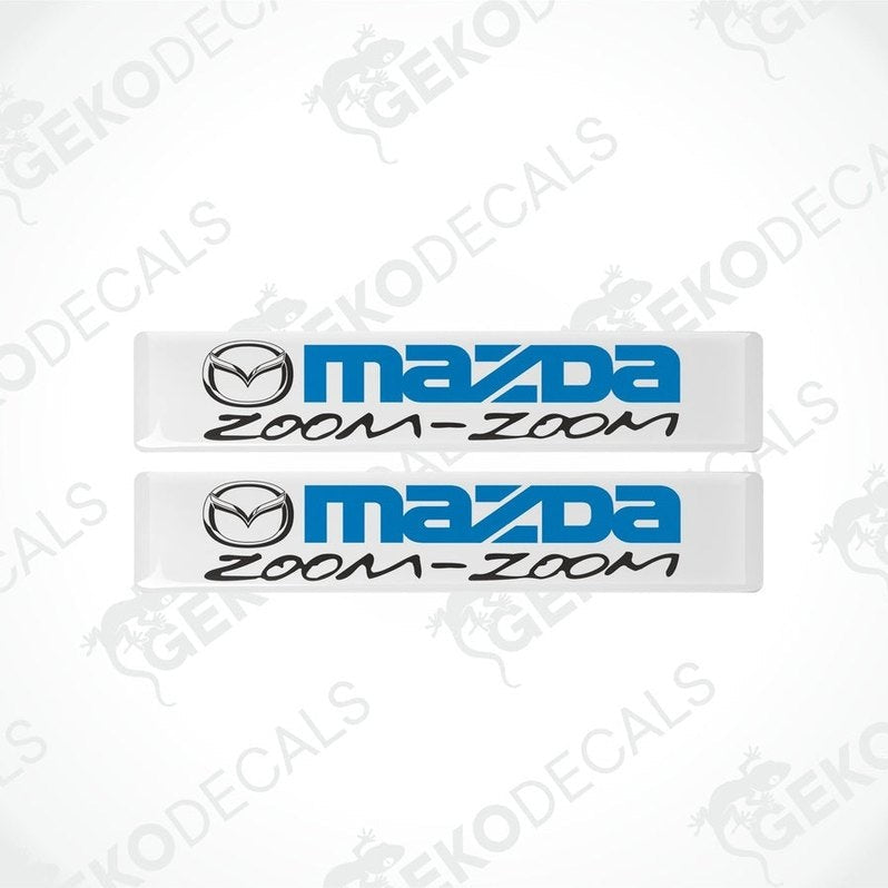 Two white vinyl stickers with the text 'MAZDA ZOOM-ZOOM' in blue.