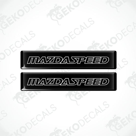 Two black rectangular car decals with 'MAZDASPEED' written in white letters.