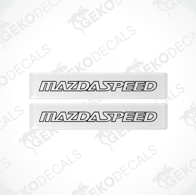 Two white rectangular car decals with 'MAZDASPEED' written in black letters.