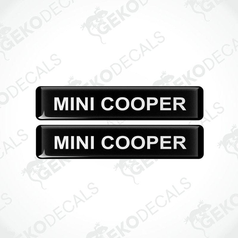 Two black rectangular car decals with the text 'MINI COOPER' in white.